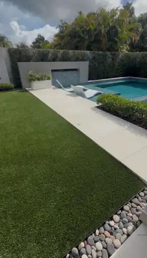 Jardín de grama artificial junto a una piscina residencial